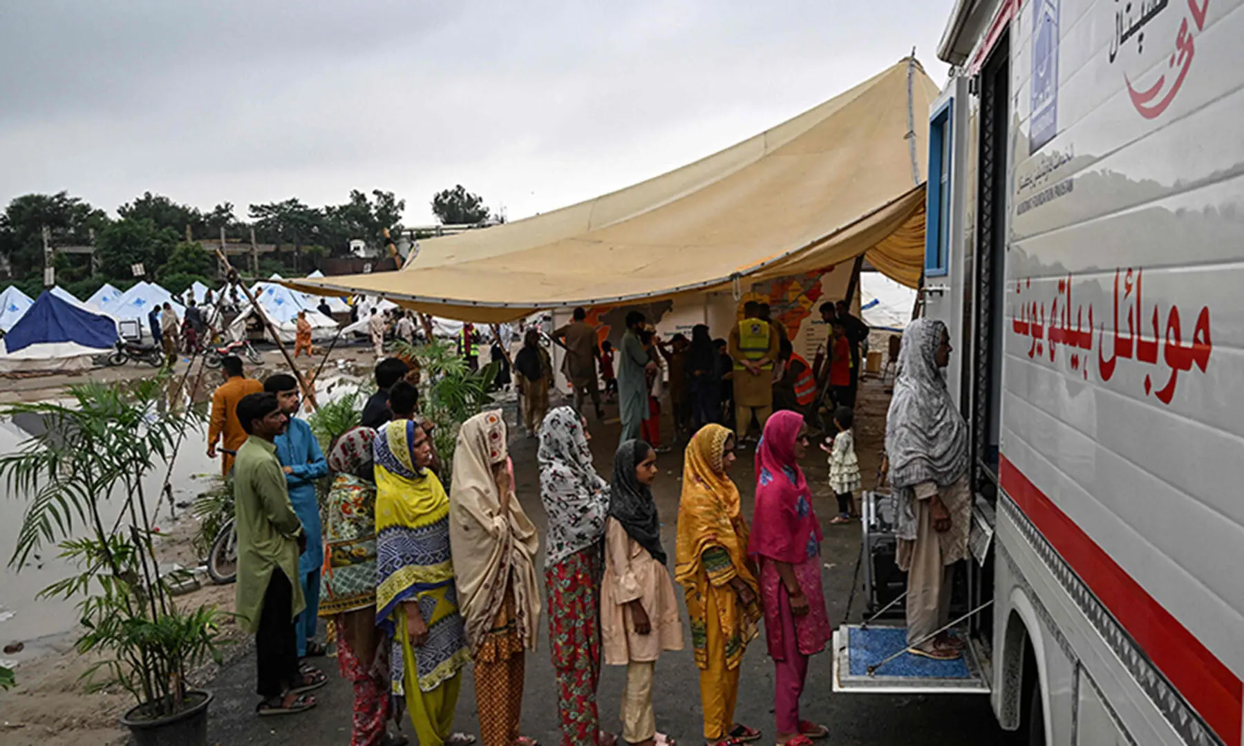 Flood victims stand in a queue outside a mobile health unit at a makeshift camp in Chung, near Lahore on August 31. — AFP