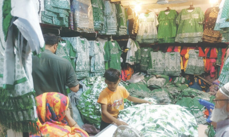 A customer is shown dresses manufactured for August 14 at a wholesale shop in the Gharyali Building in Saddar. — Photo By Mohammad Asim Rehman A customer is shown dresses manufactured for August 14 at a wholesale shop in the Gharyali Building in Saddar. — Photo By Mohammad Asim Rehman