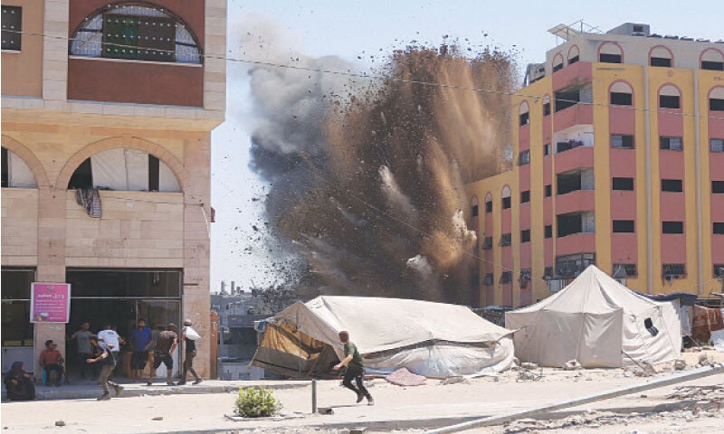 GAZA: Palestinians rush for cover after an Israeli strike on a building in Jabalia.—AFP