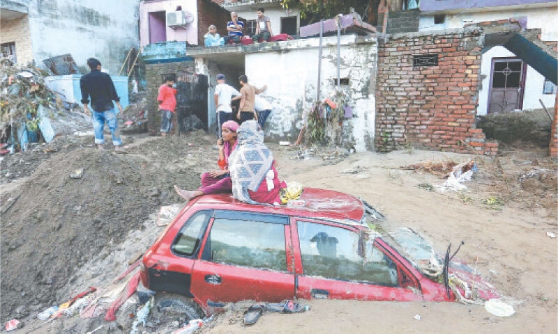 WOMEN sit over a car buried under mud and debris along the banks of the overflowing Tawi river after heavy rains induced flooding in India-held Jammu.&mdash;AFP