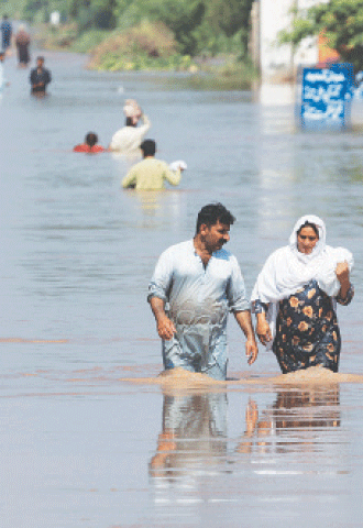 MANDI BAHAUDDIN: Residents wade through a flooded road in Qadirabad village near the River Chenab.—Reuters