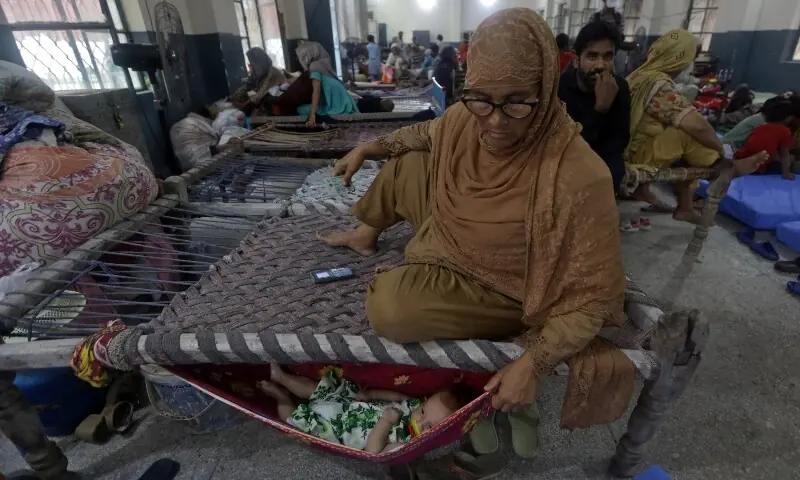 A woman, who fled with her family from flooded banks of Ravi River, watches an infant in a makeshift hammock inside a school, turned into a relief camp, in Lahore on August 31.