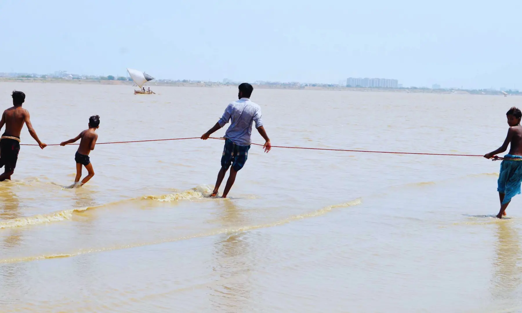 A group of young fishermen holding one end of the net while their colleagues venture into the Indus River.