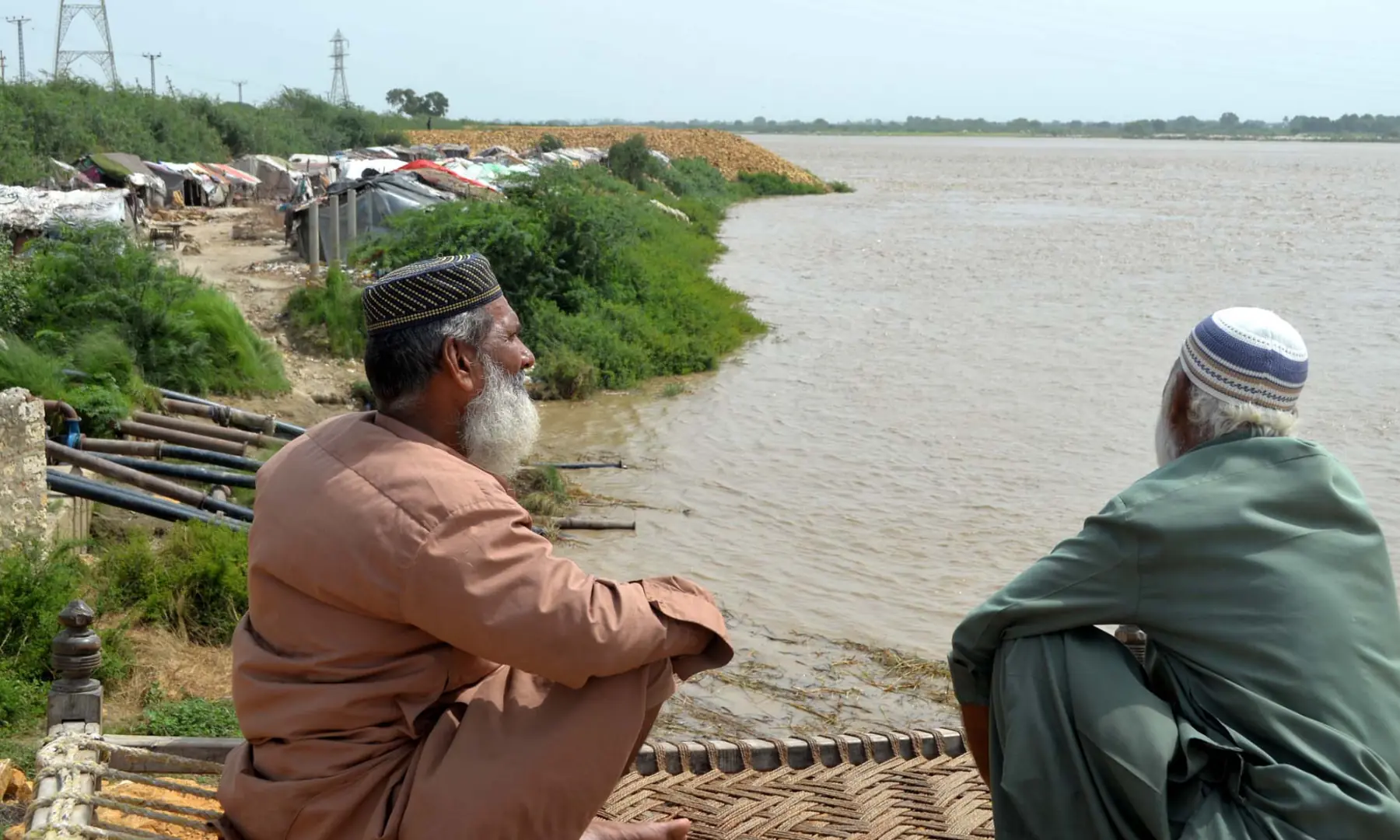 Two elderly staff members of civic agency sit near at the water facility set up near bank of Indus river for lifting of drinking water for Latifabad.