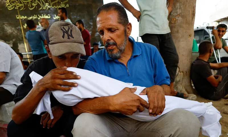 An uncle kisses a victim, held by a grandfather, where the child is part of a group of Palestinians killed in overnight Israeli strikes, according to medics, during the funeral at Al-Shifa Hospital in Gaza City, on September 5, 2025. &mdash; Reuters