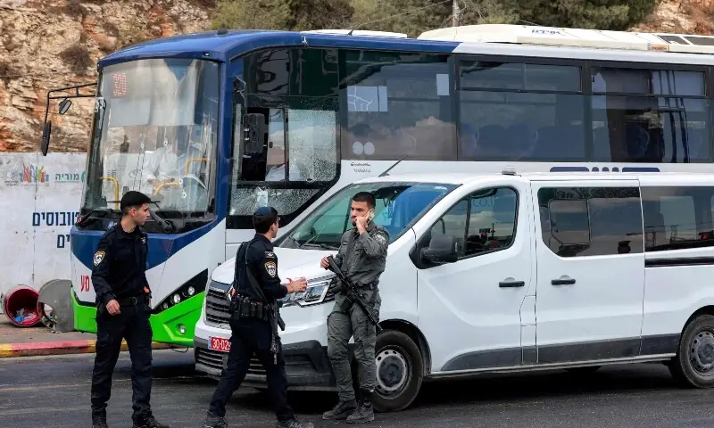 Two Israeli policemen speak to a border guard next to a bus at the scene of a shooting at the Ramot road junction in Israeli-annexed east Jerusalem on September 8. — AFP