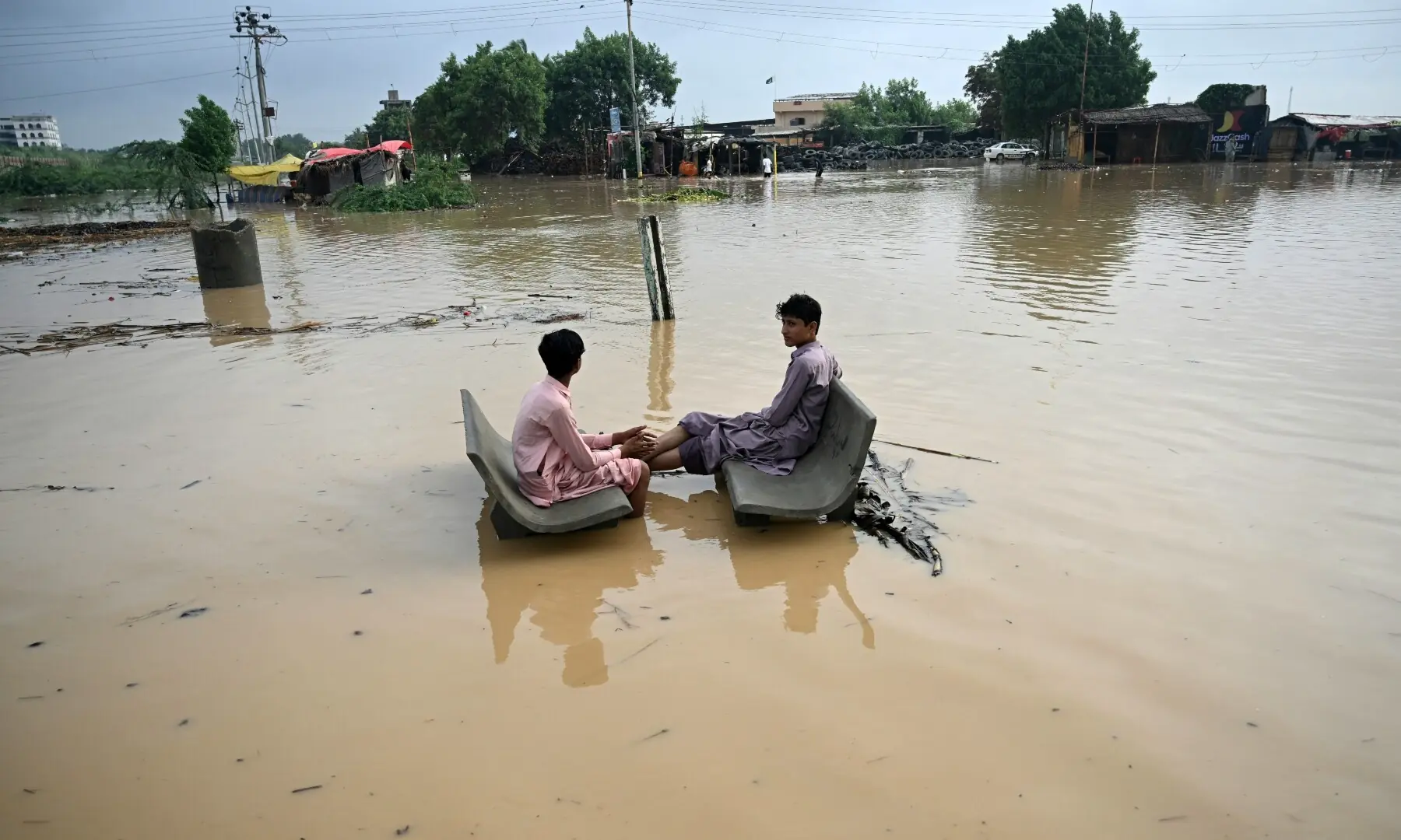 Youths rest on inundated benches along a flooded street after rainfall in Karachi on Sept 10, 2025. &mdash; AFP