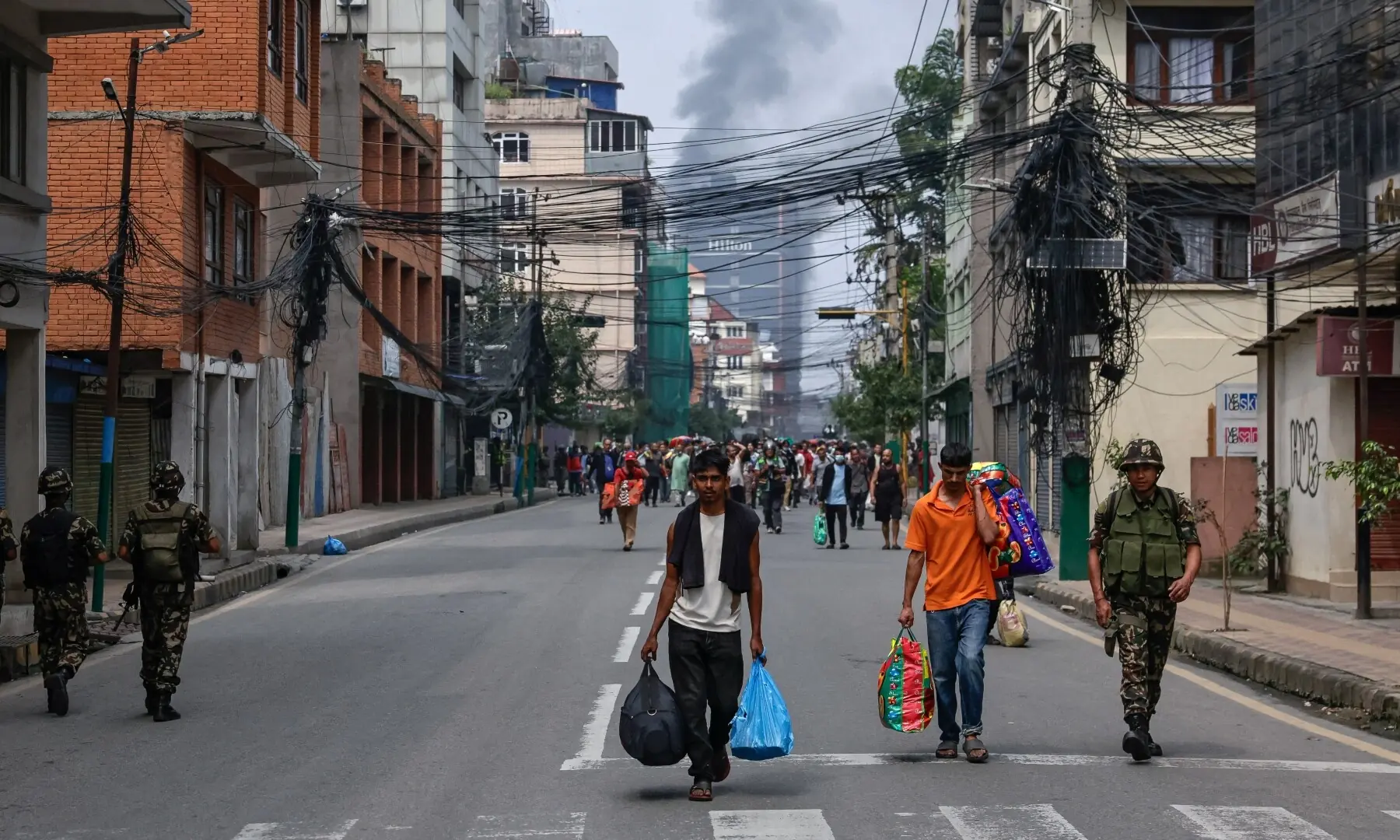 Smoke rises from the burnt Hilton Kathmandu hotel in the distance as prisoners carrying belongings walk back to Dilli Bazaar jail, next to a soldier, after escaping and being sent back by the Nepalese army, following protests. — Reuters