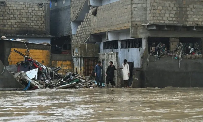 Residents stand near a damaged house as they look at a flooded street after heavy rainfall on the outskirts of Karachi, Sept 10. — AFP Residents stand near a damaged house as they look at a flooded street after heavy rainfall on the outskirts of Karachi, Sept 10. — AFP