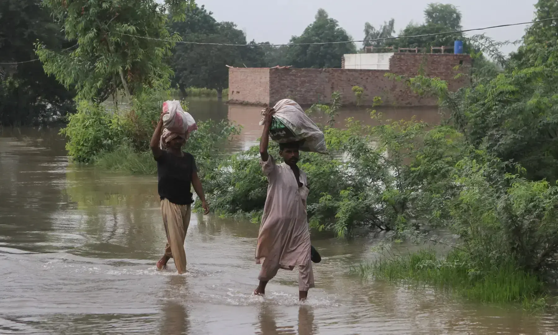 Residents carry their belongings as they wade through a flooded area, following monsoon rains and rising water levels of the Chenab River in Muzaffargarh on Sept 6, 2025. &mdash; Reuters