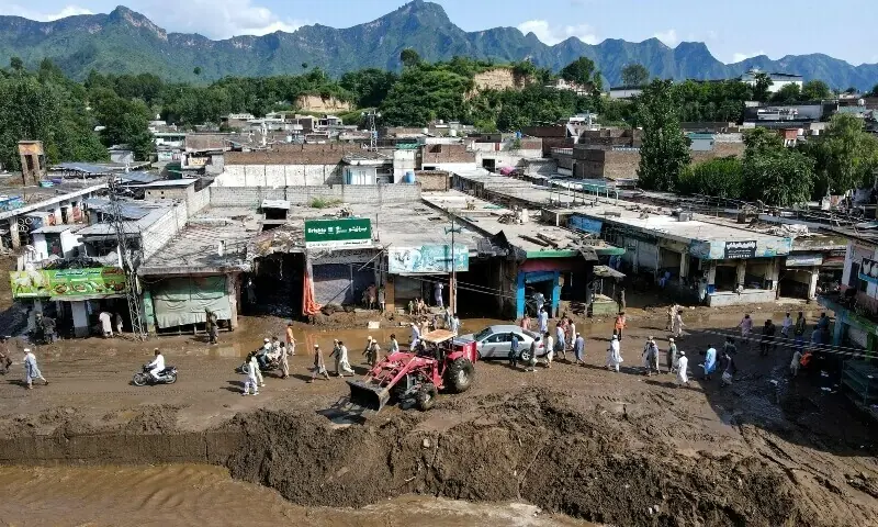 A tractor removes debris from a muddy road, after flash floods hit Buner district, August 18. — AFP A tractor removes debris from a muddy road, after flash floods hit Buner district, August 18. — AFP