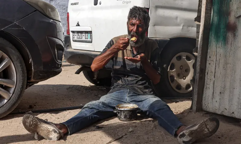 A Palestinian man sits on the ground as he eats rice that she obtained from a community kitchen in Khan Younis in the southern Gaza Strip on September 19, 2025. — AFP