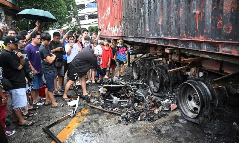 Bystanders look at a burnt motorcycle (L) and trailer van set on fire by protesters near Malacanang Palace in Manila on September 21, 2025. &mdash; AFP