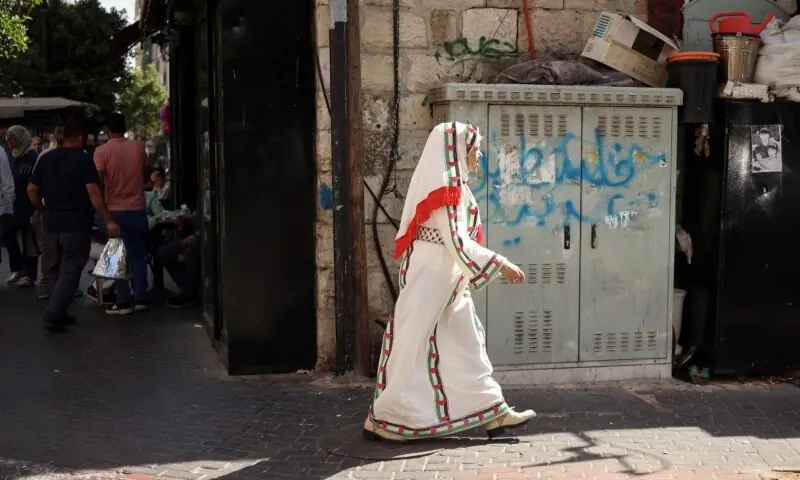 A Palestinian woman, wearing a traditional dress, walks on the sidewalk in Ramallah in the Israeli occupied West Bank on September 23. &mdash; AFP