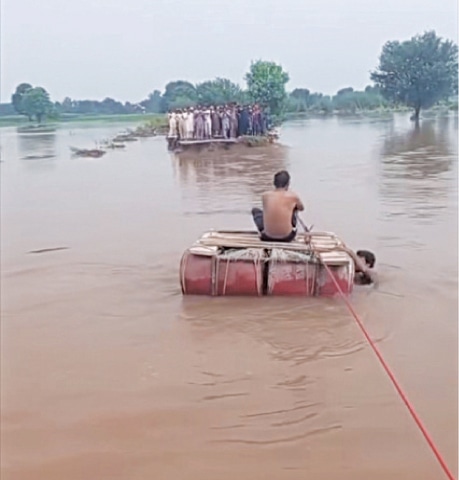  NAROWAL: This man charges Rs30 per person to carry people across the rainwater drain on his makeshift raft. &mdash; Dawn 