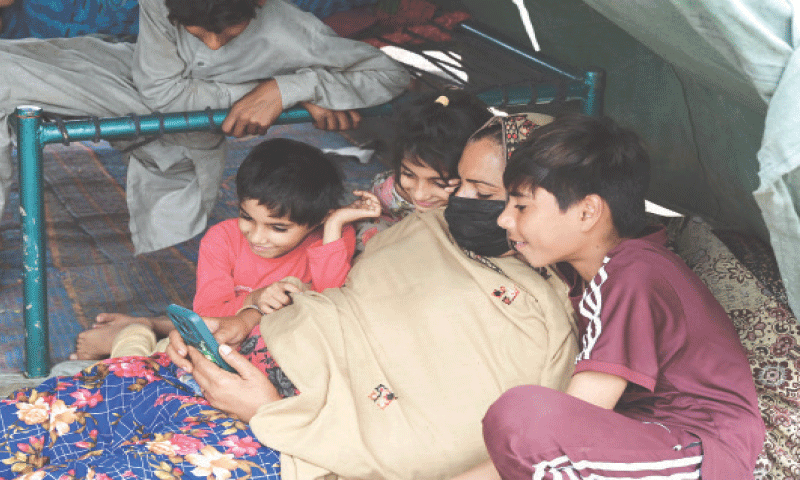 A flood-affected woman spends time by using mobile phone along with her children at a relief camp on Multan Road. &mdash; White Star