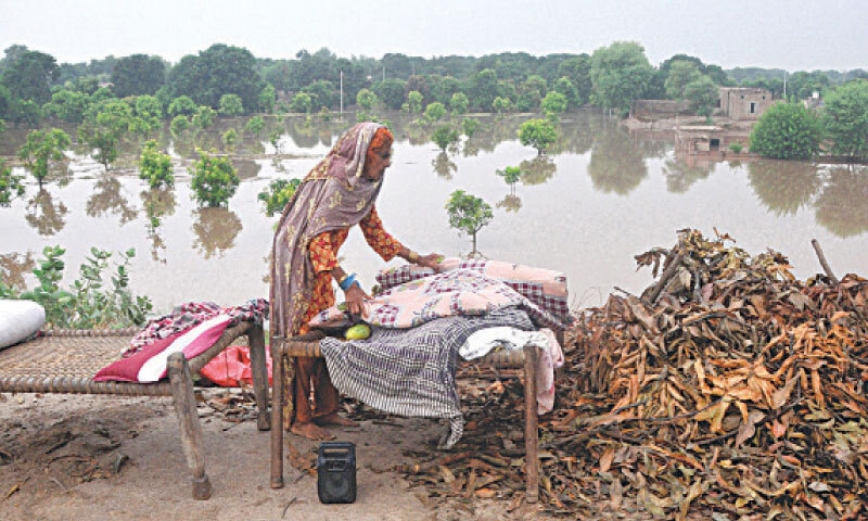 MULTAN: An elderly woman makes her bed next to an elevated road, after her locality &mdash; seen in the background &mdash; was submerged by floodwaters from the Chenab.&mdash;APP