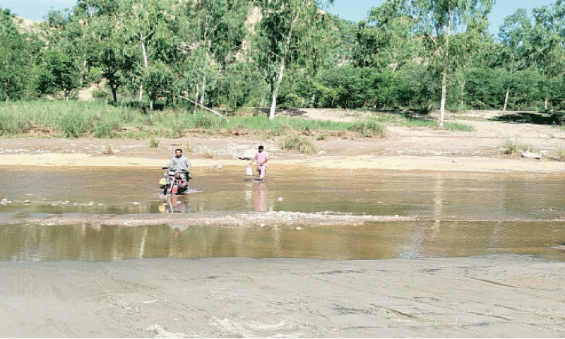 Commuters wade through Ghabir Nullah in the absence of a bridge. &mdash; Dawn
