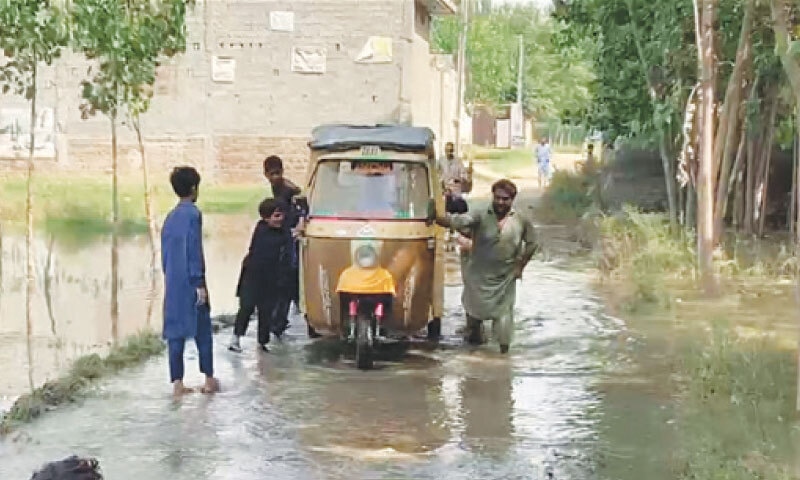 Residents push a rikshaw through the water inundating Kausarabad area of Charsadda. &mdash; Dawn