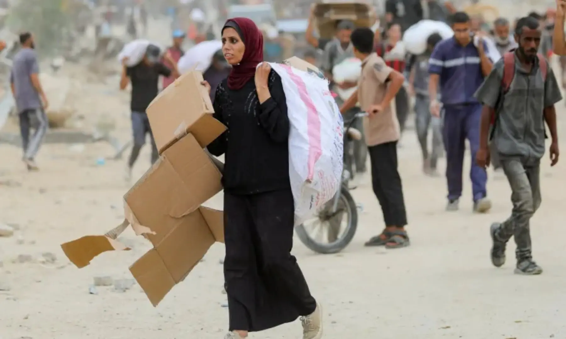  A woman carries empty cardboard boxes as Palestinians receive aid supplies from the US-backed GHF, in the central Gaza Strip, on August 1, 2025 — Reuters  