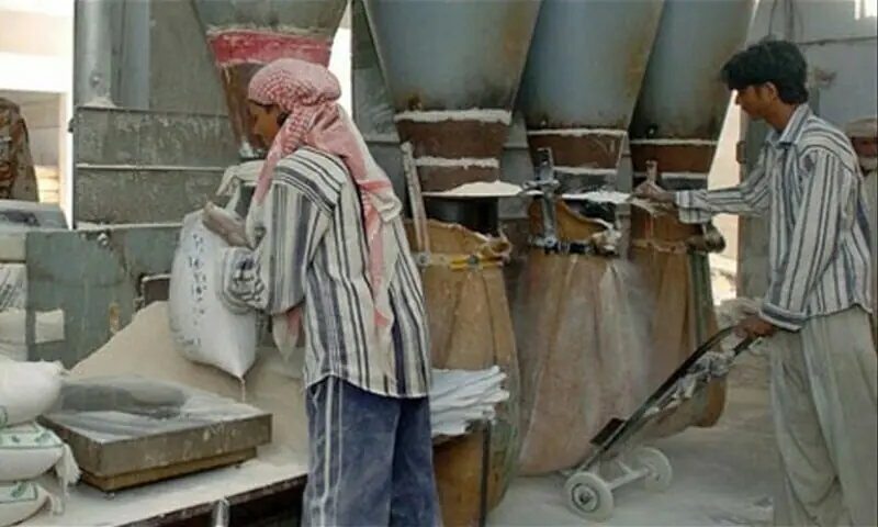 Image shows workers filling bags with wheat flour at a mill. &mdash; File photo