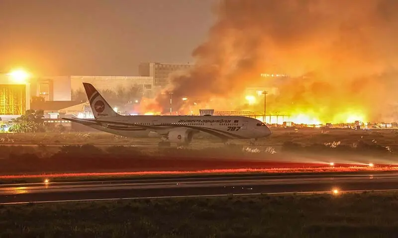 An airliner stands on the tarmac as firefighters try to extinguish a fire that broke out in the cargo section of Hazrat Shahjalal International Airport in Dhaka, Bangladesh on October 18. &mdash; AFP
