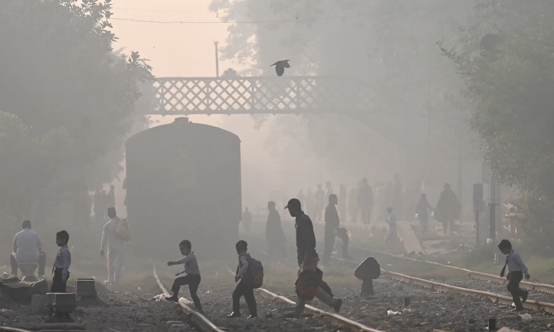 People cross a train track amid pollution in Lahore on October 25. — AFP