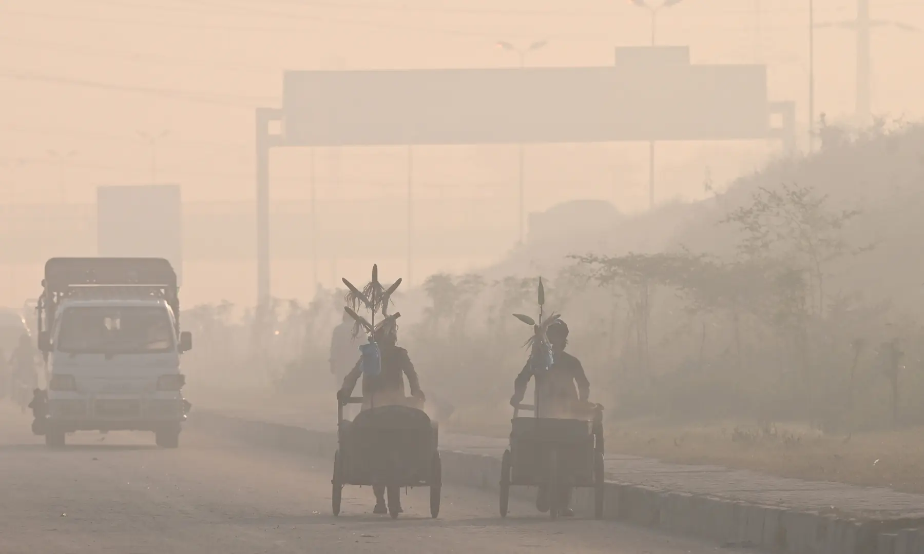 Vendors (right) push their carts as they sell corn on a smog-shrouded street in Lahore on October 25. — AFP