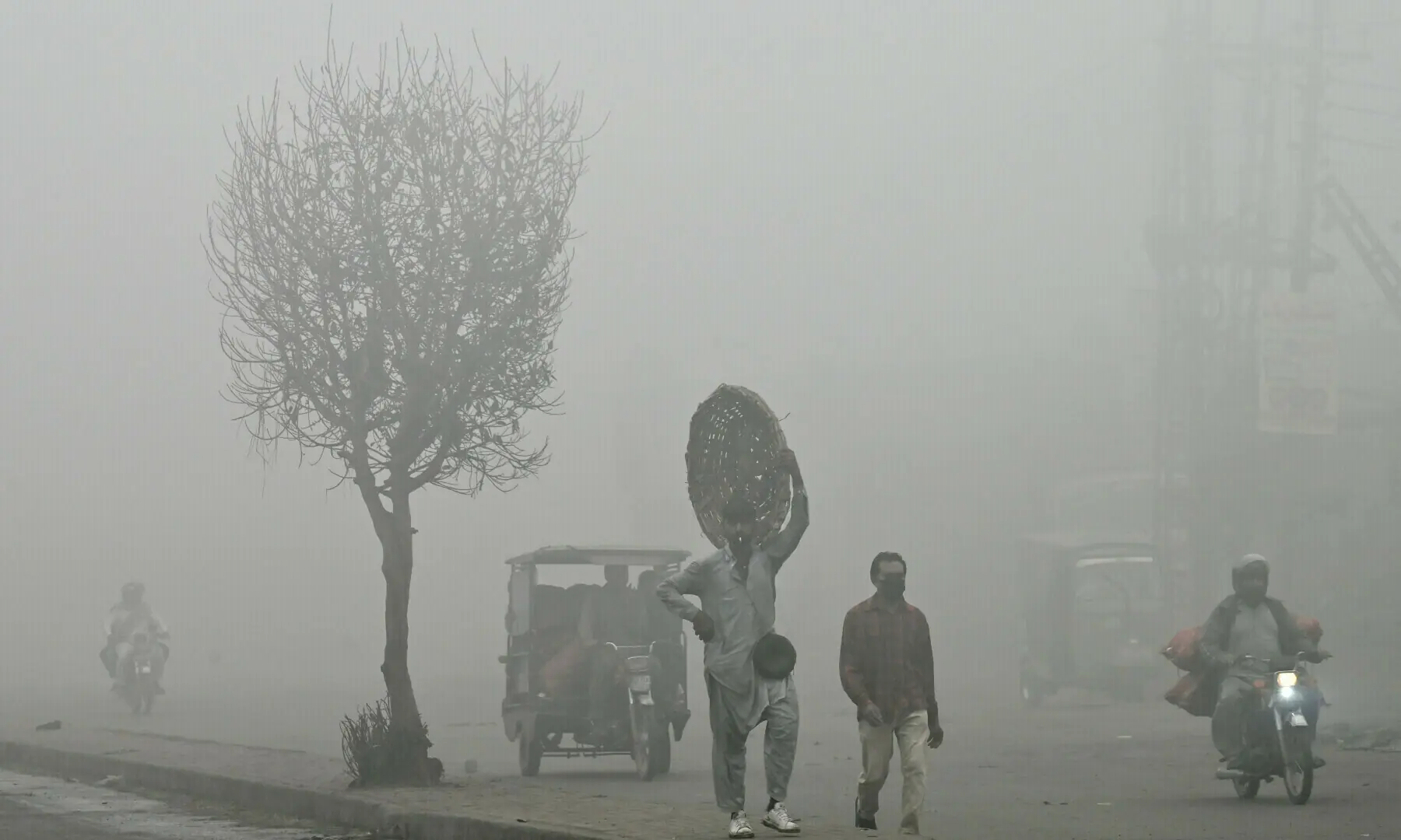 Pedestrians walk along a road engulfed in thick smog in Lahore on Nov 11, 2024. &mdash; AFP/File