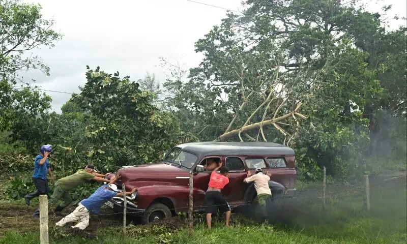 People push a vehicle stuck in the mud on a road blocked by a tree that was toppled by strong winds, in the aftermath of Hurricane Melissa, in Santiago, Cuba, October 29, 2025. &mdash; Reuters/Norlys Perez