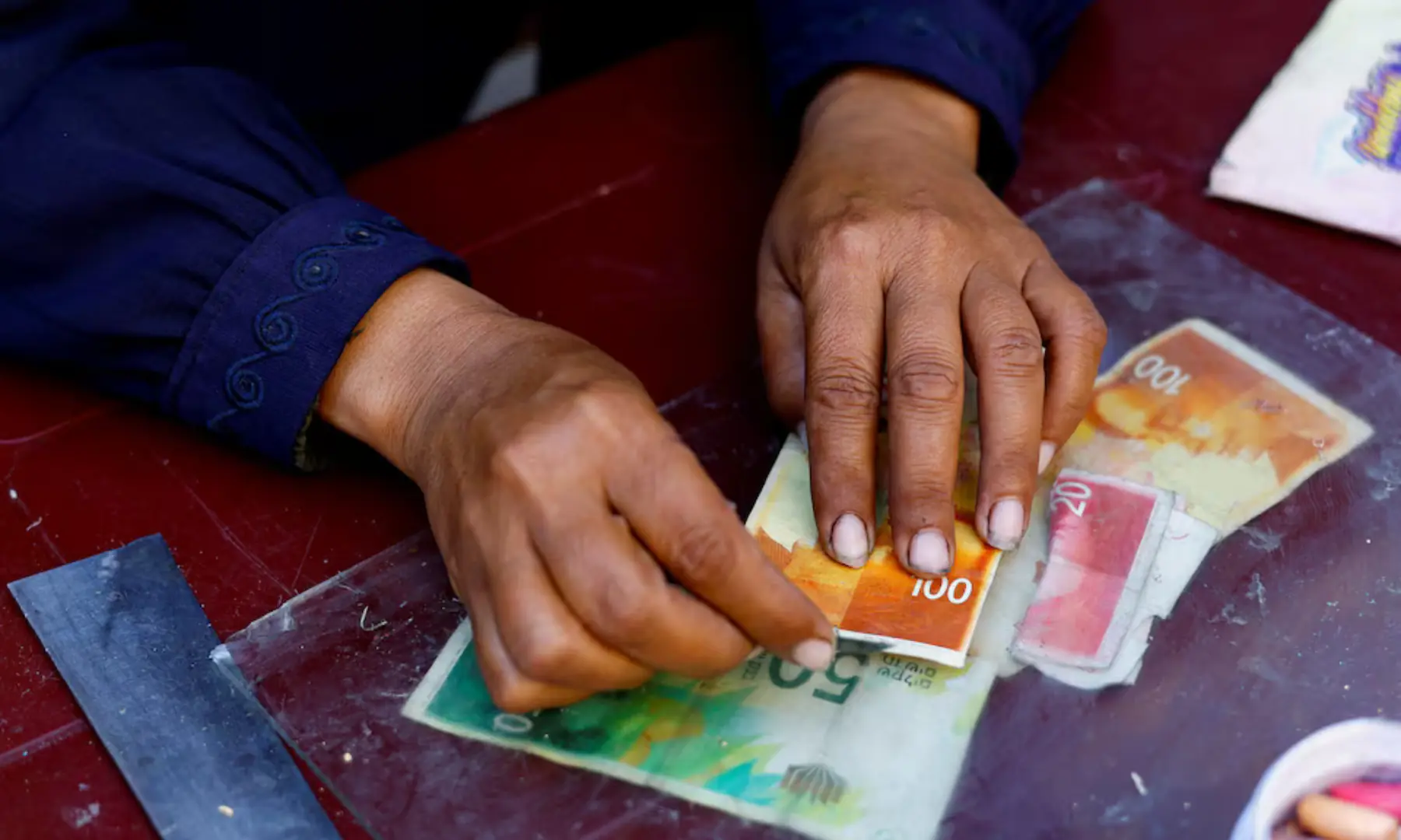 Palestinian woman Manal al-Saidi repairs damaged banknotes on the side of a street, amid a cash crisis, in Nuseirat, central Gaza Strip on October 27, 2025. &mdash; Reuters