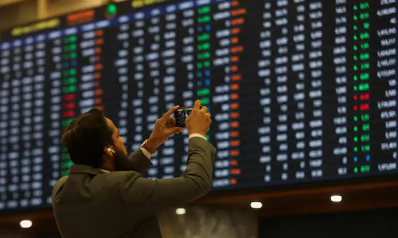 A man uses a mobile phone as he takes a photo of the electronic board displaying share prices during a trading session at the Pakistan Stock Exchange, in Karachi, Pakistan, on November 28, 2023. &mdash; Reuters/File