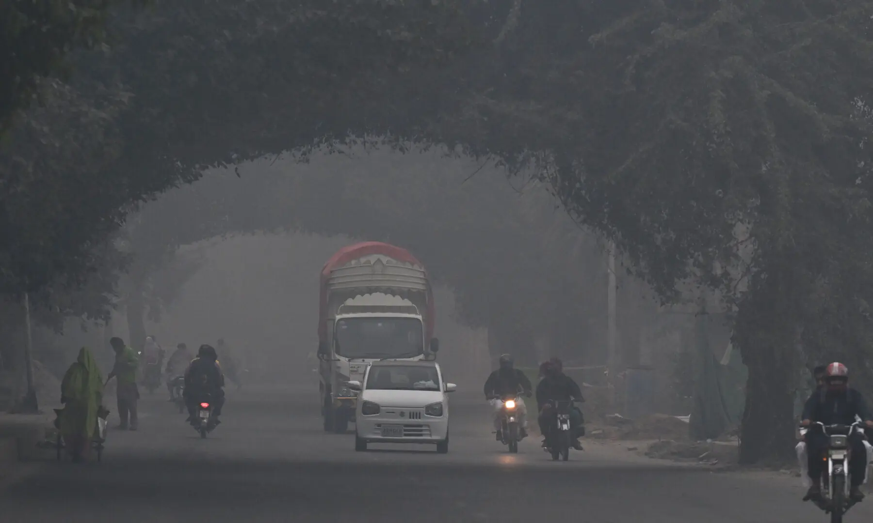 Commuters ride along a street amid dense smog in Lahore on Nov 1, 2025. &mdash; AFP