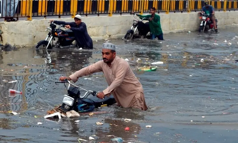 People wade through a flooded street after heavy monsoon rains in Karachi on July 26.  &mdash; AFP