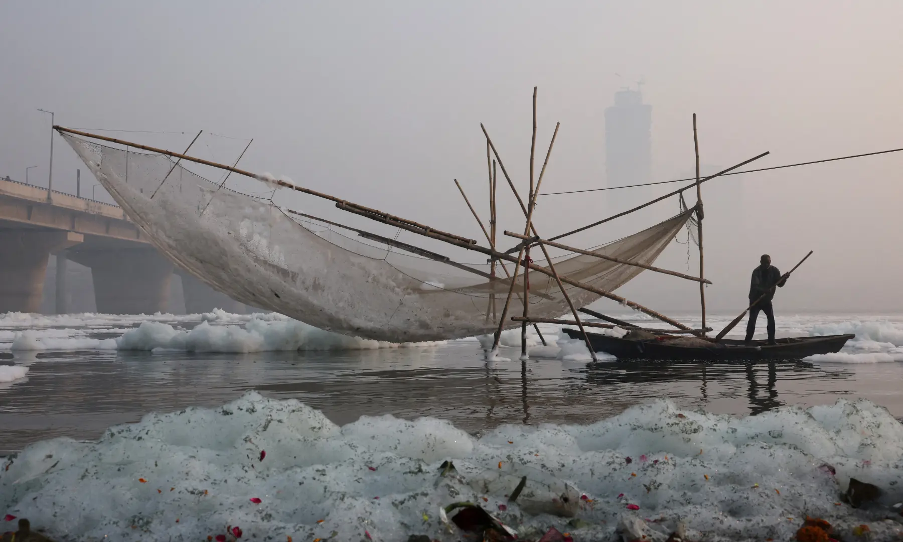 A fisherman on a boat stands next to a fishing net covered with foam, on the polluted Yamuna river, on a smoggy morning amid ongoing air pollution in New Delhi, India, on November 21. &mdash; Reuters