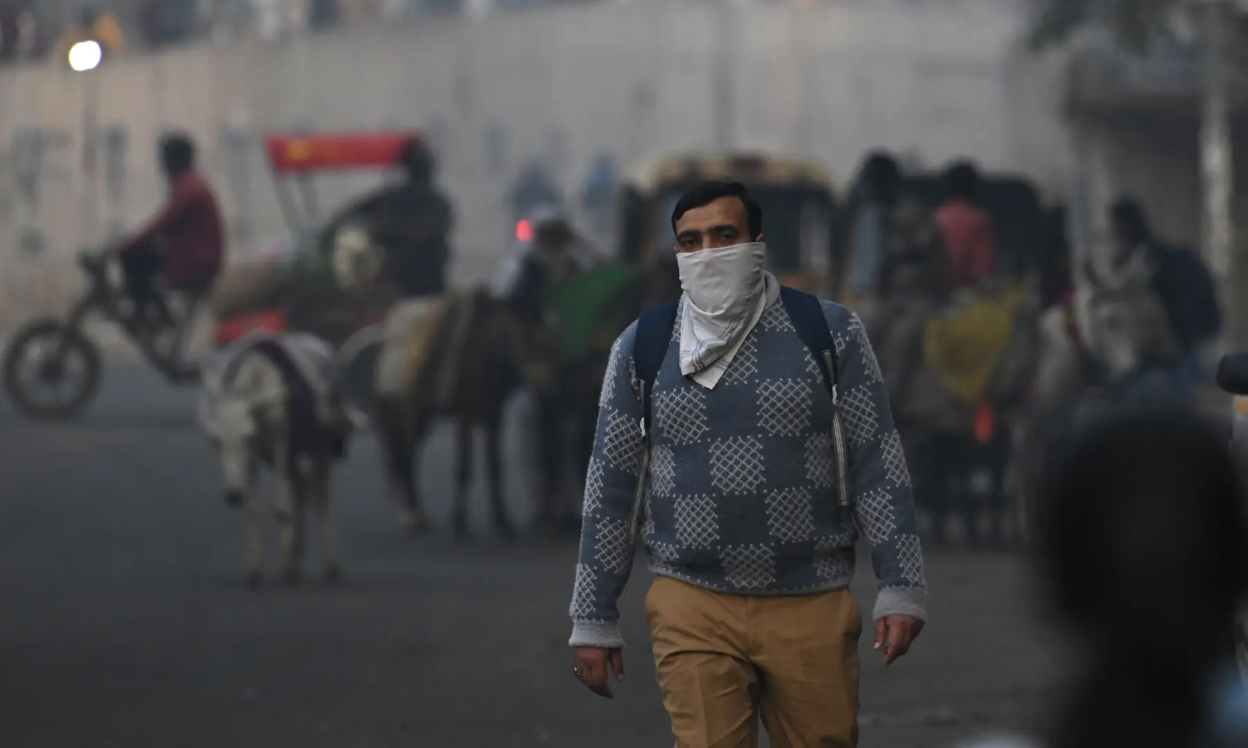 A man covering his face with a handkerchief walks along a road amid smoggy conditions in New Delhi on November 21. &mdash; AFP