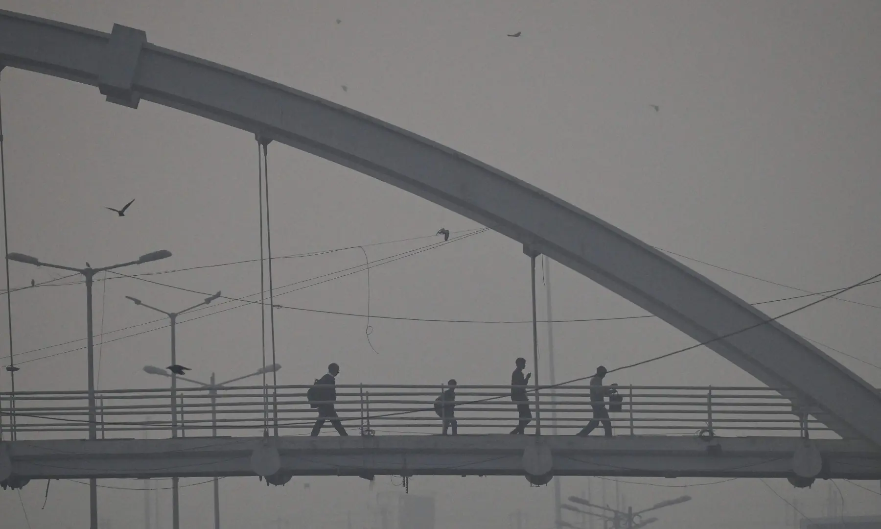 Commuters walk across a footbridge amid smoggy conditions in New Delhi on November 21. &mdash; AFP