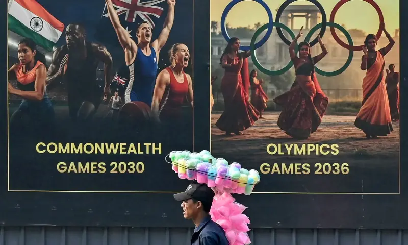 A cotton candy seller walks past a billboard featuring potential sporting events in Ahmedabad on November 26, 2025. &mdash; AFP