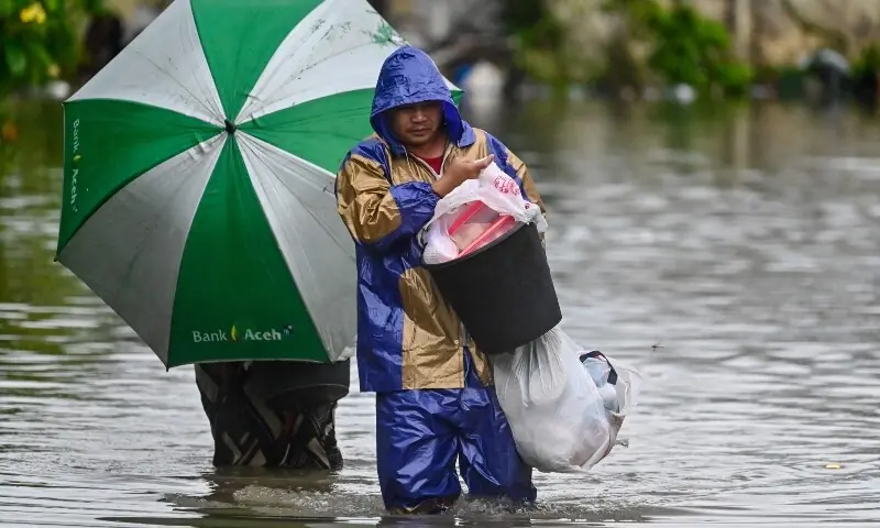 A man and a woman carry their belongings as they wade through the floodwaters on an inundated street following heavy rain at a residential area of Darul Imarah on the outskirts of Banda Aceh on November 27, 2025. — AFP A man and a woman carry their belongings as they wade through the floodwaters on an inundated street following heavy rain at a residential area of Darul Imarah on the outskirts of Banda Aceh on November 27, 2025. — AFP