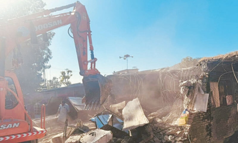 A machine demolishes an illegal structure along Karakoram Highway in Shinkiari on Friday. — Dawn