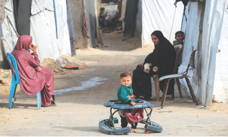 A child stands in an old stroller as a Palestinian woman looks on at Nuseirat camp in central Gaza Strip.&mdash;AFP