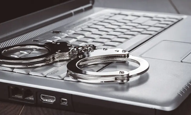 A file photo of handcuffs resting on top of a laptop. ─ File photo