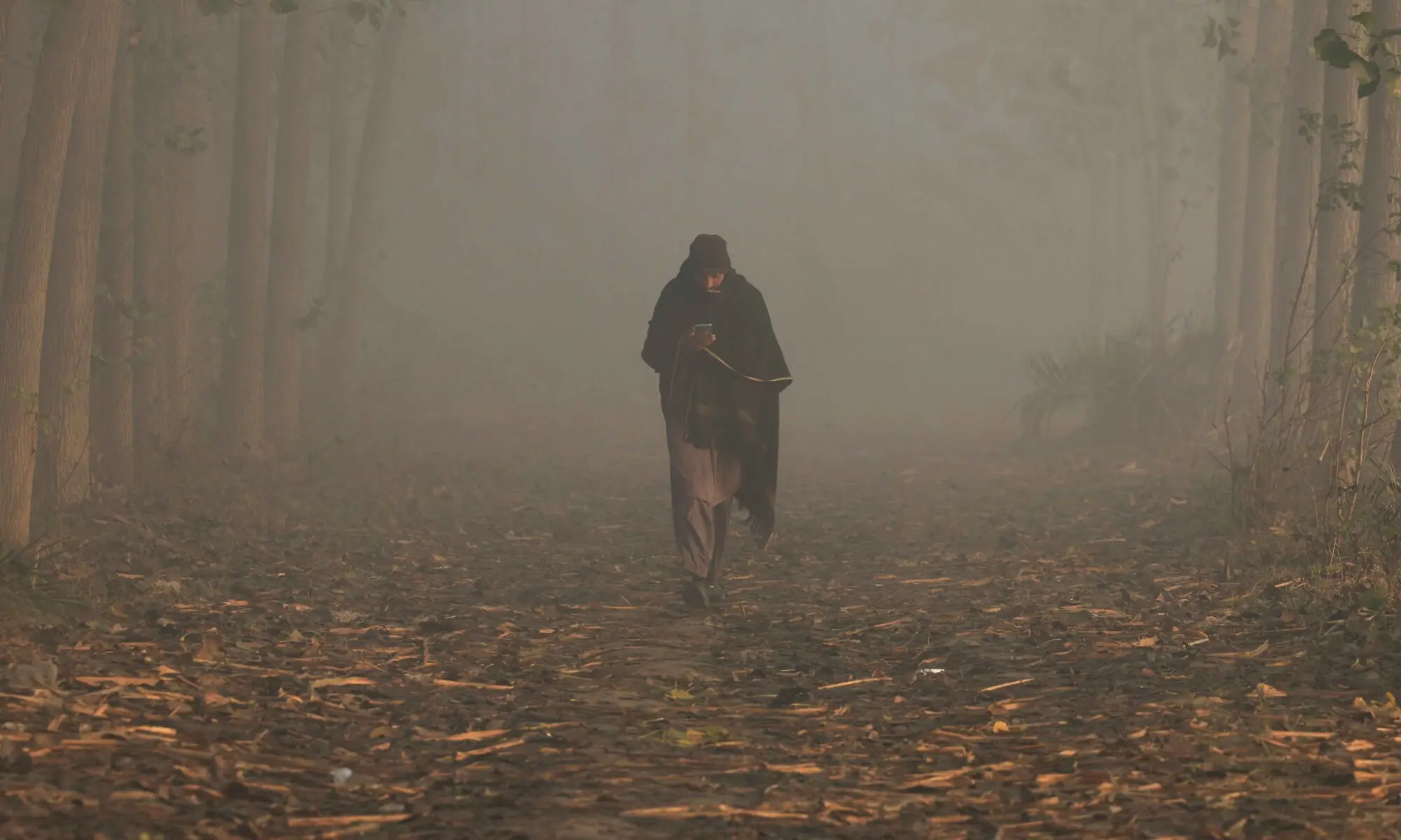 A man uses his mobile phone as he walks amid smog and air pollution during morning hours, in Peshawar on  November 28, 2025. &mdash; Reuters