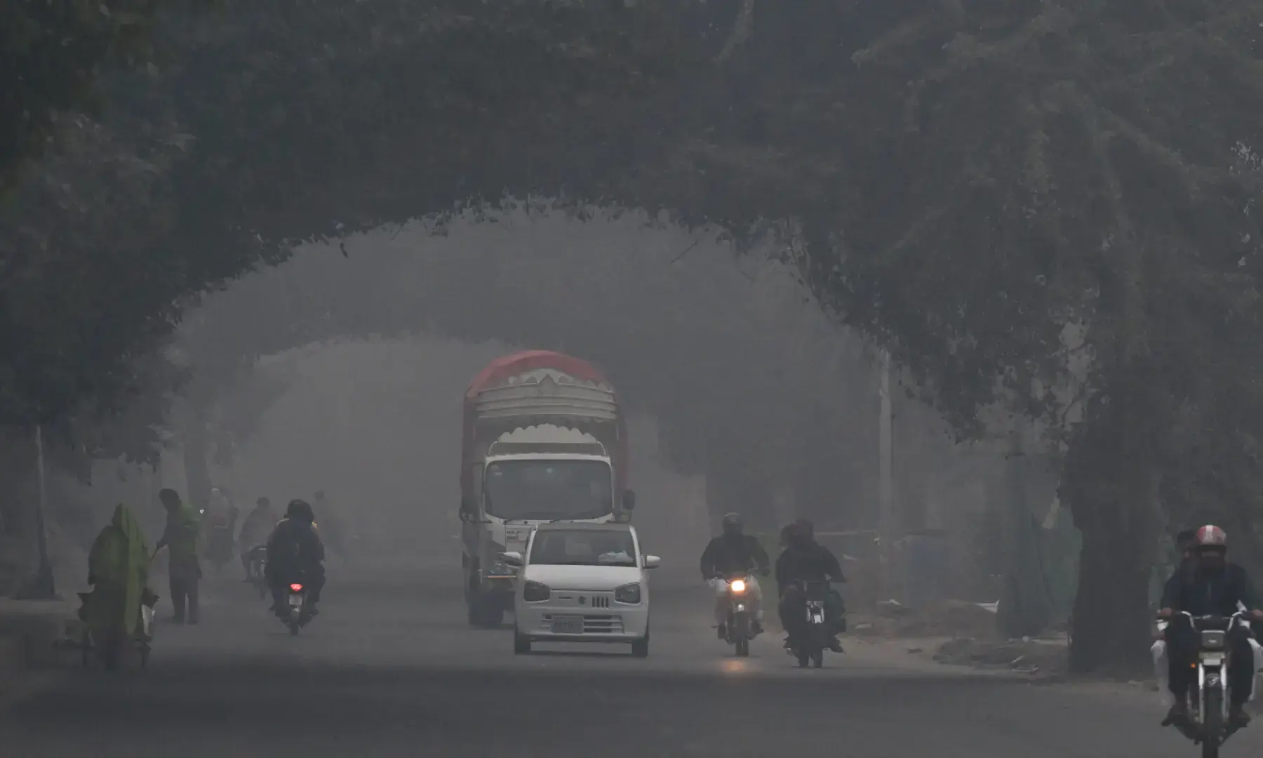 Commuters ride along a street amid dense smog in Lahore on Nov 1, 2025. &mdash; AFP/File