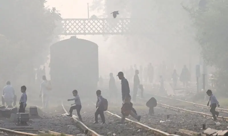 People walk across a railway track amid smoggy conditions in Lahore on Oct 25. &mdash; AFP