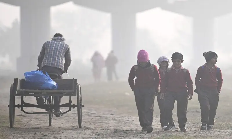 Schoolchildren walk through a field on a smoggy winter morning in New Delhi on December 17. —AFP