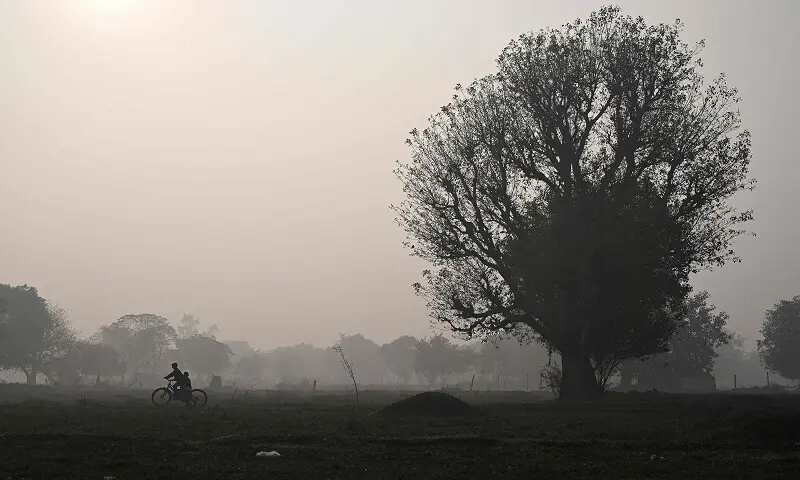 Children ride a bicycle across a field on smoggy winter morning in New Delhi on December 17. &mdash;AFP