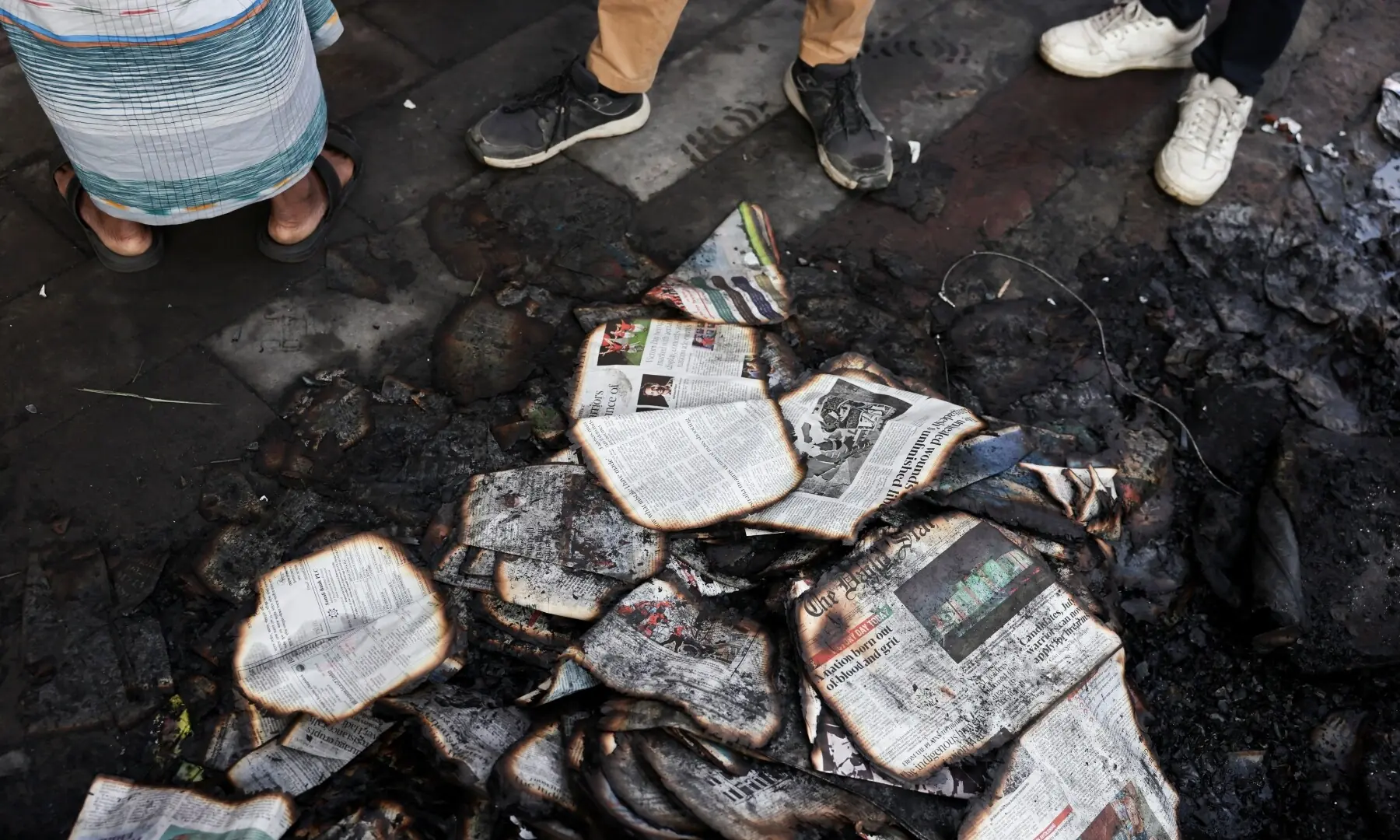 People stand next to burnt newspapers in front of the Daily Star building, following the death of Sharif Osman Hadi, a student leader, who had been undergoing treatment in Singapore after being shot in the head, in Dhaka, Bangladesh, December 19, 2025. &mdash; Reuters