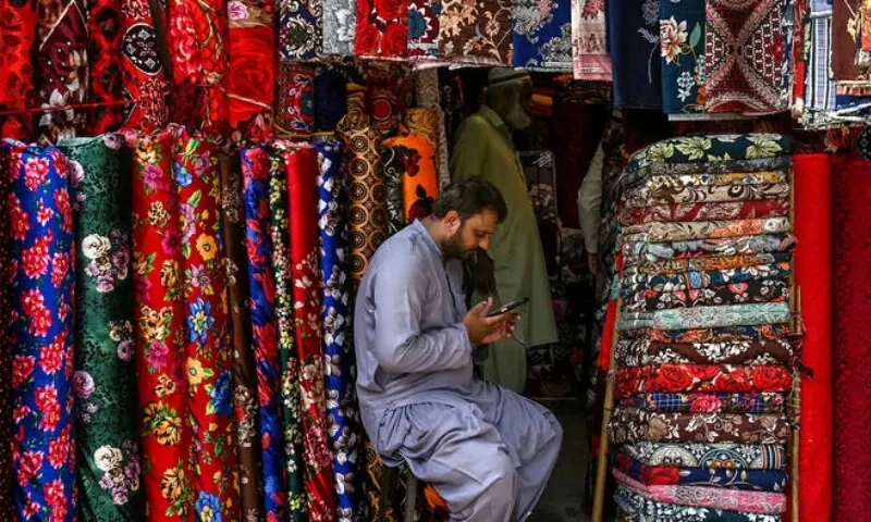 A vendor uses a mobile phone as he waits for customers at a market in Lahore on July 31, 2025. &mdash; AFP