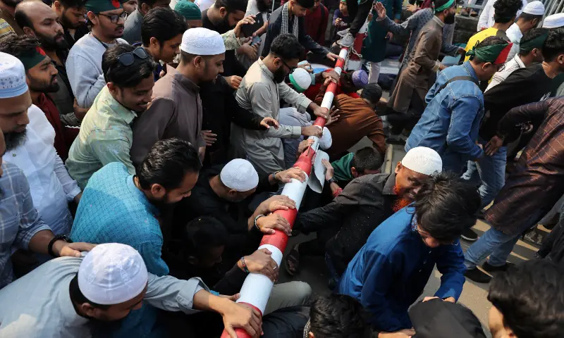 People pass underneath of a boom barrier to attend the funeral prayer for Sharif Osman Hadi, a student leader, who died after being shot in the head, at the Parliament building area of Manik Mia Avenue, in Dhaka, Bangladesh on December 20, 2025. &mdash; Reuters